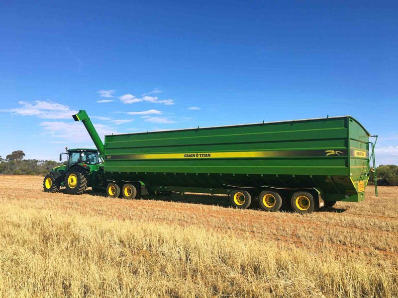 Green tractor pulling a large green grain cart in a field.